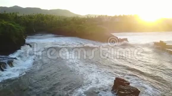 日落时分巴厘岛沿海地区的空中摄影有美丽的太阳光海浪岩石海岸线和海滩视频的预览图