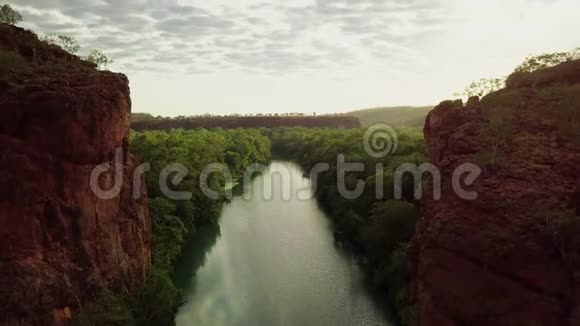 日出时在巨大的红色岩壁之间飞过河流进入山谷绿洲视频的预览图