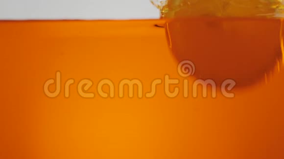 鲜橙片在淡色背景下随着溅沫和气泡落入橙水或茶中视频的预览图