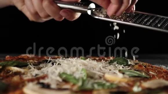 专业厨师把帕尔马干酪涂在烤架上在黑色背景下搭配意大利腊肠的披萨上掉落的奶酪视频的预览图