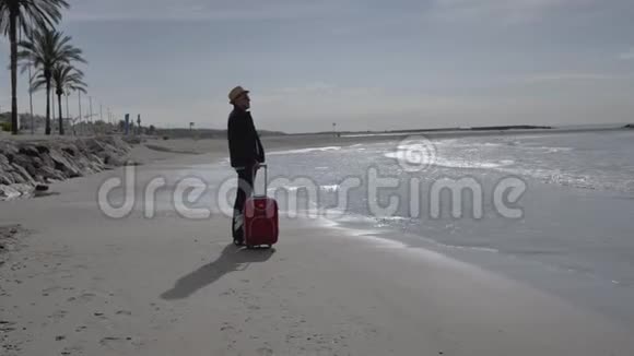 一位游客来到海边站在岸边高兴地拿起一个红色的手提箱视频的预览图