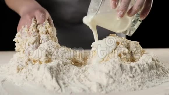 专业的面包师从玻璃杯中倒入奶油与面粉和鸡蛋混合在一堆面粉中加深面团的概念视频的预览图