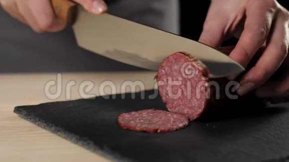 专业厨师用锋利的金属刀在黑色背景下的黑板上切割腊肠面团揉捏的概念视频的预览图