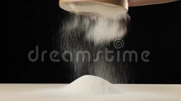 专业的面包师用黑色背景的木筛筛面粉掉落的白色颗粒视频的预览图