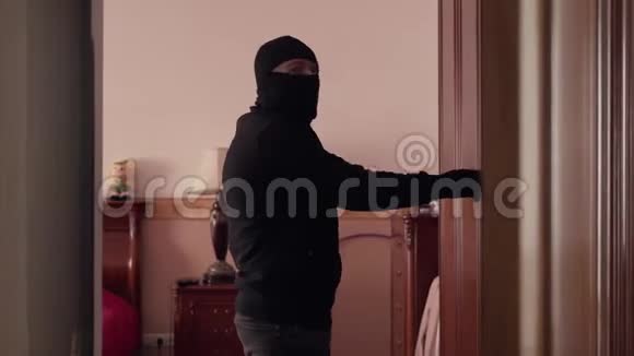 穿着黑色衣服和巴拉克拉瓦的小偷打开大卧室的衣柜想要钱偷东西的家伙视频的预览图