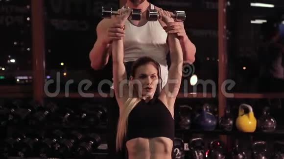 年轻女子和她的健身教练在健身房用哑铃视频的预览图