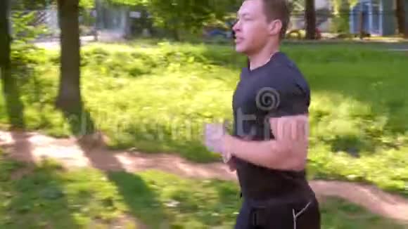 年轻的运动员正在城市公园慢跑在夏季阳光明媚的日子侧视视频的预览图