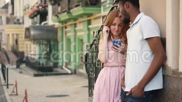 一个年轻的女人给她的男朋友一个耳机一起听一首歌视频的预览图