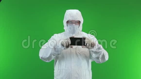 一个穿着防护服和面罩的男人在手机上拍摄了一段绿色背景视频视频的预览图