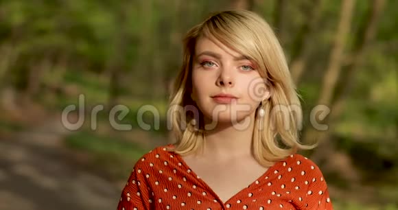 年轻自信的女人的肖像一头金发直视着摄像机站在美丽的公园里视频的预览图