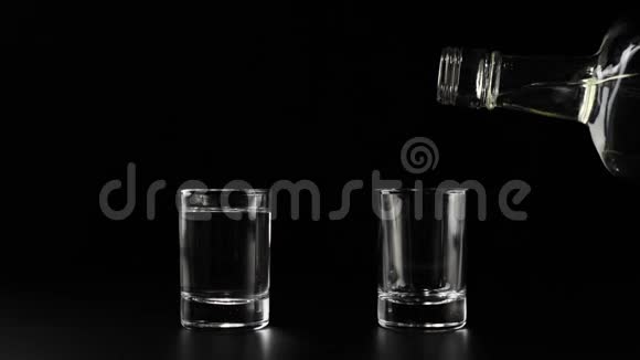 黑桌上的两副眼镜用手将伏特加龙舌兰酒或清酒从平杯中倒入桌上的空杯中视频的预览图
