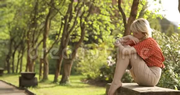 年轻迷人的女人一头华丽的金色头发正在美丽的夏季公园里休息她坐在长凳上视频的预览图