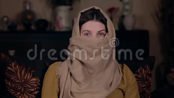一位年轻漂亮的阿拉伯女人坐在一张罩袍的扶手椅上写下她的视频社会媒体视频的预览图