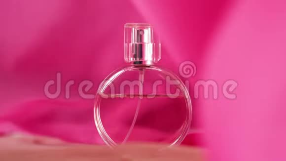 椭圆形表面瓶与粉红色香水或精油是在米色织物上粉红色的织物在空中飘来飘去视频的预览图