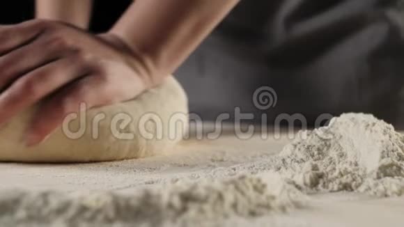 专业的面包师把面团揉在靠近面粉堆的木桌上背景是黑色的烹饪比萨饼的概念视频的预览图