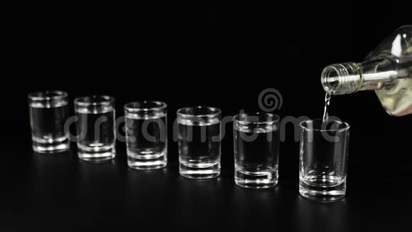 桌子上有六副眼镜用手将伏特加龙舌兰酒或清酒从平瓶中倒入黑桌上的空杯中视频的预览图