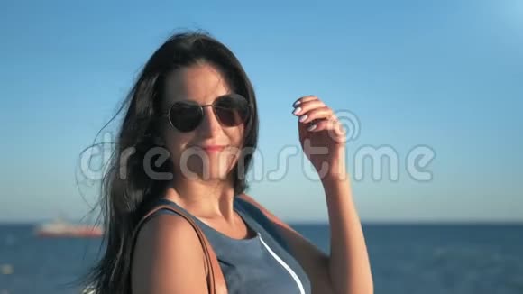 日出时分在自然海岸和天空的环绕下戴着时髦太阳镜的快乐女孩轻松地调情视频的预览图