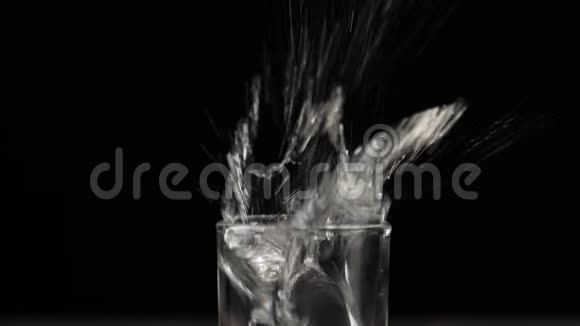 冰块掉下来溅起水花然后在黑底黑桌上用伏特加龙舌兰酒或清酒泡成玻璃杯视频的预览图