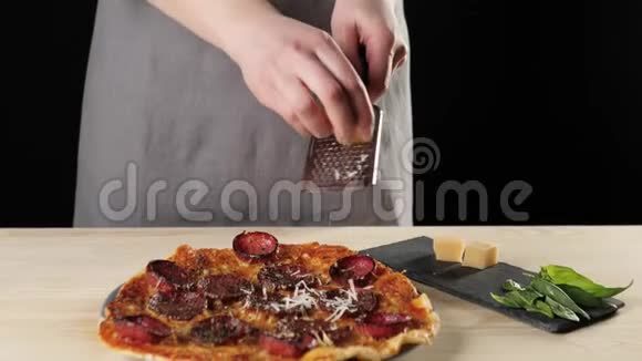 专业厨师把帕尔马干酪涂在烤架上在黑色背景下搭配意大利腊肠的披萨上掉落的奶酪视频的预览图