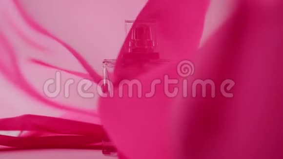 白色桌子上放着带有青色香水或精油的扁平表面瓶粉红色的织物在空中飘来飘去视频的预览图