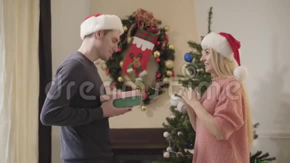 一个戴着圣诞帽的迷人的白种女人在看礼物做不高兴的表情并把礼物还给男人视频的预览图