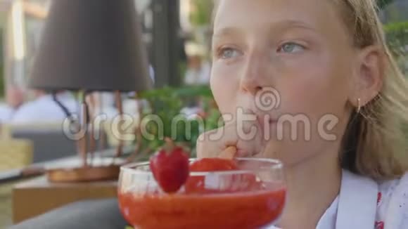 快乐的少女在夏天的咖啡馆喝草莓鸡尾酒脸上挂着微笑的女孩享受草莓视频的预览图