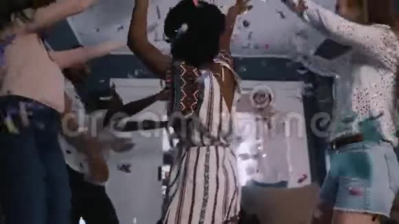 低角快乐的年轻美丽的非洲女人在五彩纸屑下和朋友们在有趣的多民族聚会上慢动作跳舞视频的预览图