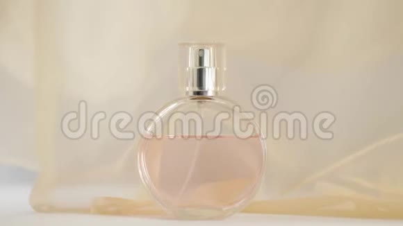 白色的桌子上摆着一瓶粉红色的香水或精油米色织物在空气中飘来飘去视频的预览图