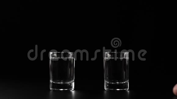 两杯伏特加龙舌兰酒或清酒放在黑桌子上手拿着桌子上黑色背景的杯子视频的预览图