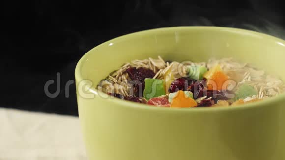 新鲜健康食品新鲜燕麦片与蜜饯葡萄干和蔓越莓在桌子上烟在食物中蔓延视频的预览图