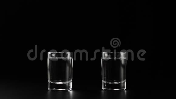 冰块随着溅起的水花和气泡掉落到两个玻璃杯中杯中有伏特加龙舌兰酒或黑桌上的清酒视频的预览图