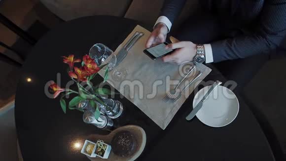商人坐在餐厅的餐桌旁使用他的智能手机视频的预览图
