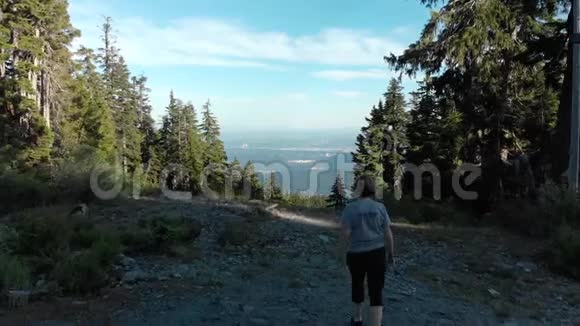 无人机拍摄了一名中年妇女在山林徒步旅行小径上行走俯瞰一座城市视频的预览图