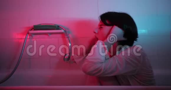 紫色浴室里尖叫的黑发女孩愤怒的年轻女子正坐在充满水的浴缸里呼喊着抱着她视频的预览图