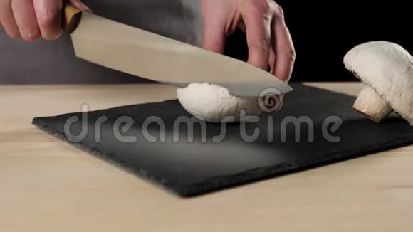 专业厨师用一把锋利的金属刀在黑色背景的黑板上切蘑菇面团揉制的概念视频的预览图