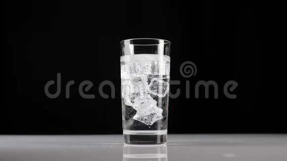 冰块在玻璃杯中旋转和漂浮玻璃杯中有气泡或苏打水背景为黑色呆在家里的概念视频的预览图