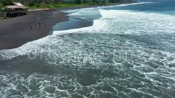 三个冲浪者沿着海滩漫步从上面可以看到黑色的沙景视频的预览图