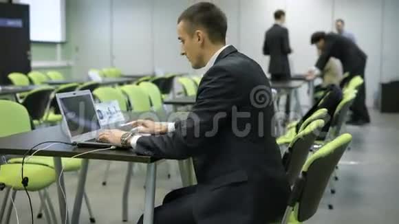 一位身穿商务服戴着昂贵手表的年轻人正在使用笔记本电脑他坐在黑色书桌后面的绿色椅子上视频的预览图