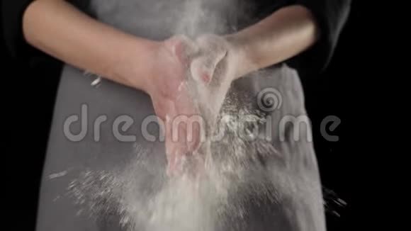 专业厨师拍拍手面粉粉飞黑色背景上掉落的白色颗粒面团揉捏的概念视频的预览图