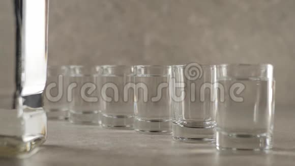 桌子上有六副眼镜用手将伏特加龙舌兰酒或清酒倒入大理石桌上的空杯中视频的预览图