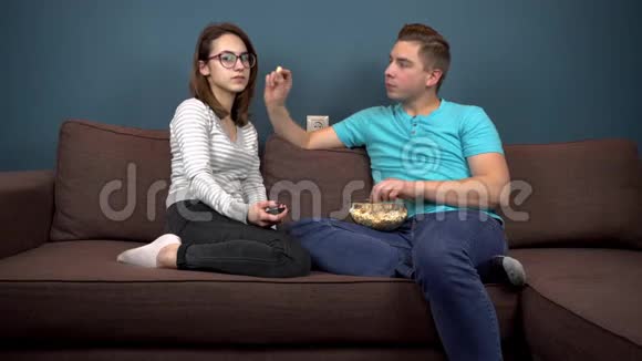 男人喂女人爆米花那家伙把爆米花放进女人嘴里一对夫妇在看电视坐在沙发上视频的预览图