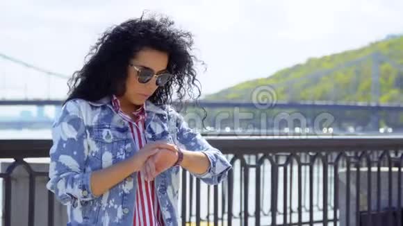 戴墨镜的年轻女子看着手表在堤边等人视频的预览图