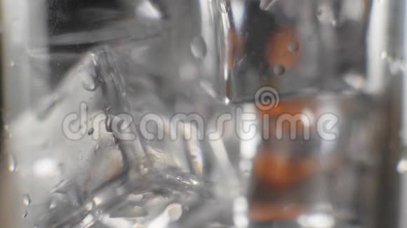 新鲜橙汁的特写镜头在闪闪发光的冷冰块上流动在一个高杯中滴着水滴形成气泡填满它视频的预览图