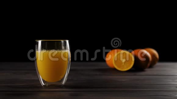 在一个装有新鲜橙汁的双壁玻璃杯中冰块在木桌上溅出大量的气泡视频的预览图
