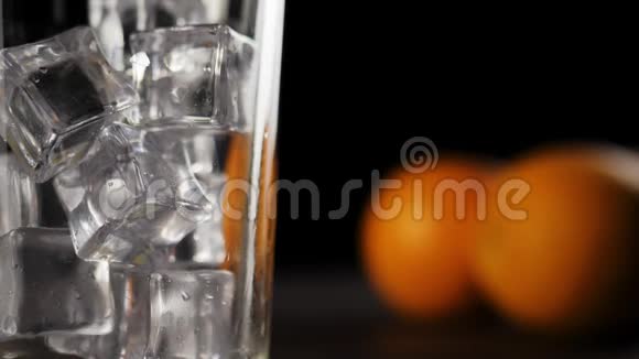 新鲜橙汁的特写镜头在闪闪发光的冷冰块上流动在一个高杯中滴着水滴形成气泡填满它视频的预览图