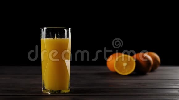 在一个带有新鲜橙汁的仙后座玻璃中掉落的大块冰块在一张木桌上溅起水花和气泡视频的预览图