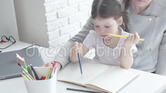 幸福的家庭妈妈保姆教可爱的小女孩在桌子旁画画妈妈帮小女儿学画画视频的预览图