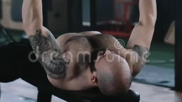 后视年轻的高加索举重运动员男子努力工作沉重的哑铃躺在健身房的长凳上视频的预览图