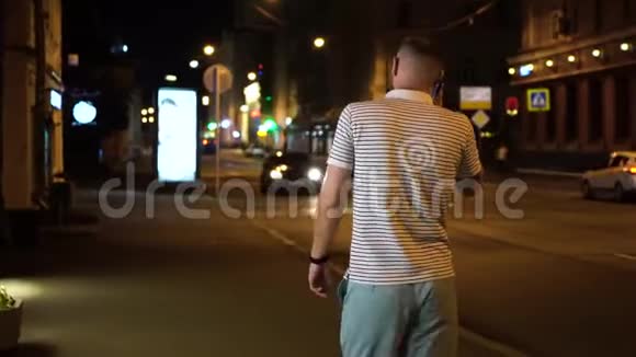 留胡子的男人穿着条纹白黑t恤和绿色短裤晚上在街上散步用手机聊天视频的预览图