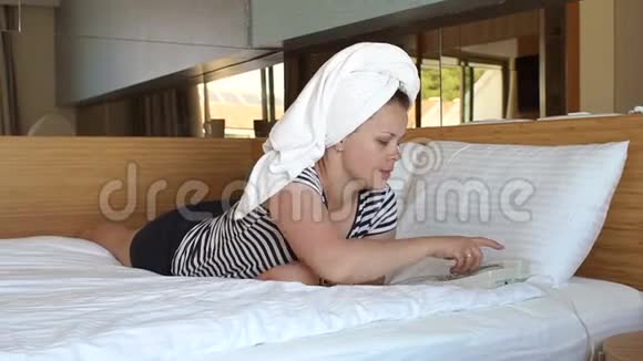 一个头上戴毛巾的女孩躺在酒店的床上在电话里交谈视频的预览图